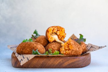Mozzarella peyniri ile doldurulmuş pirinç topları ve ahşap bir tabakta kızartılmış. Hafif arkaplan.