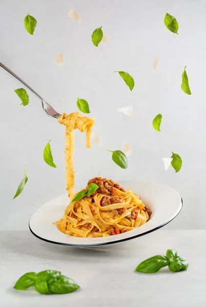 Bolonez eti ve domates soslu İtalyan makarnası yemek. Uçan fesleğen yaprakları ve parmesan peynirinin huzuru. Havada asılı dinamik bir fotoğraf. Açık gri arkaplan.