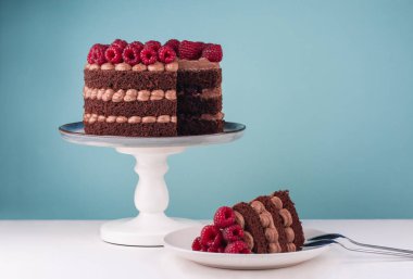 Beyaz masa ve mavi arka planda ahududu kremalı çikolatalı doğum günü pastası. Tabakta çocuk oyuncağı. Boşluğu kopyala.