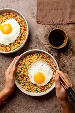 Kızarmış yumurta yiyen sebzeli, yeşil bezelyeli, dolma biberli, havuçlu ve kabaklı soya soslu, çubuklu bir kız. Üst görünüm, kahverengi tablo yüzeyi.