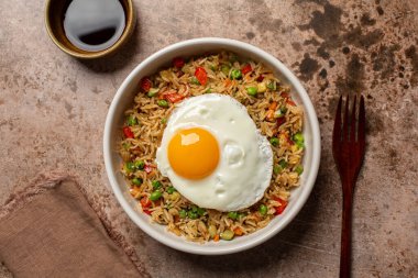 Sebzeli kızarmış yumurta, yeşil bezelye, dolma biber, havuç ve kabak, soya sosu ve çatalla servis edilir. Üst görünüm, kahverengi tablo yüzeyi.