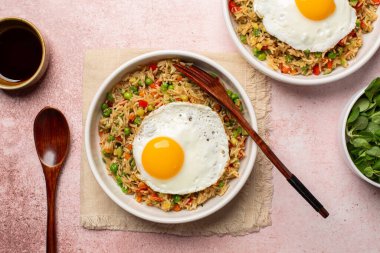 Kızarmış yumurta ve sebze, yeşil bezelye, dolma biber, havuç ve kabakla birlikte soya sosu, salata ve çatalla servis edilen öğle yemeği. Üst manzara, pembe masa yüzeyi.