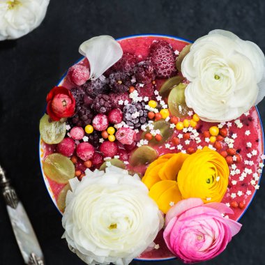 Kahvaltı Detoks Pink Smoothie muz ve orman meyveleri kase tepesinde Dondurulmuş çilek ve tipik çiçekler, koyu arka plan, üstten görünüm