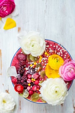 Kahvaltı Detoks Pink Smoothie muz ve orman meyveleri kase, dondurulmuş çilek ve tipik çiçekler, açık renkli ahşap, üstten görünüm ile tepesinde