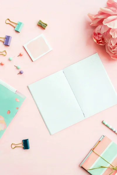 Empty Notebook for writing Dreams and Ideas, with different Stationery, and Big Pink Peony flowers laying on Pink background. Top View. Idea of Girly Office settings. Flat lay style.