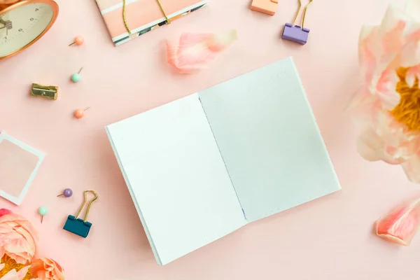 Empty Notebook for writing Dreams and Ideas, with different Stationery, and Big Pink Peony flowers laying on Pink background. Top View. Idea of Girly Office settings. Flat lay style.