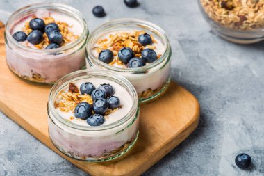 Ev yapımı Granola ve gri arka plan üzerinde cam kavanozlara yaban mersini taze doğal yoğurt kahvaltıdan