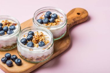 Ev yapımı Granola ve açık pembe renkli cam kavanozlara yaban mersini taze doğal yoğurt kahvaltıdan