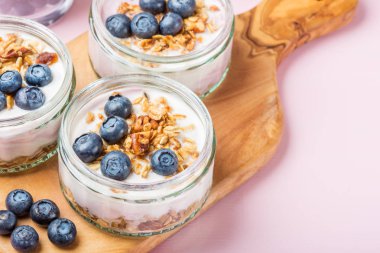 Ev yapımı Granola ve açık pembe renkli cam kavanozlara yaban mersini taze doğal yoğurt kahvaltıdan