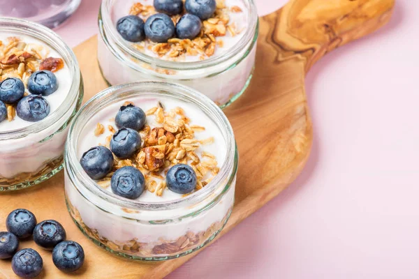 Ev yapımı Granola ve açık pembe renkli cam kavanozlara yaban mersini taze doğal yoğurt kahvaltıdan