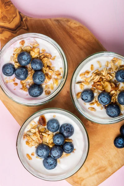 Ev yapımı Granola ve açık pembe renkli cam kavanozlara yaban mersini taze doğal yoğurt kahvaltıdan