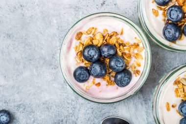 Ev yapımı Granola ve gri arka plan üzerinde cam kavanozlara yaban mersini taze doğal yoğurt kahvaltıdan