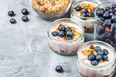 Ev yapımı Granola ve gri arka plan üzerinde cam kavanozlara yaban mersini taze doğal yoğurt kahvaltıdan