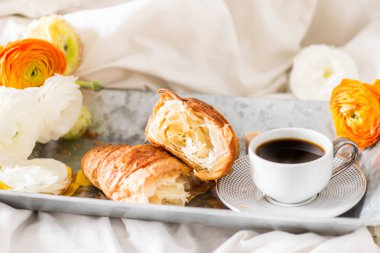 Gri tepsisindeki yakın tipik çiçekler taze kruvasan ve kahve Kupası yatakta kahvaltı