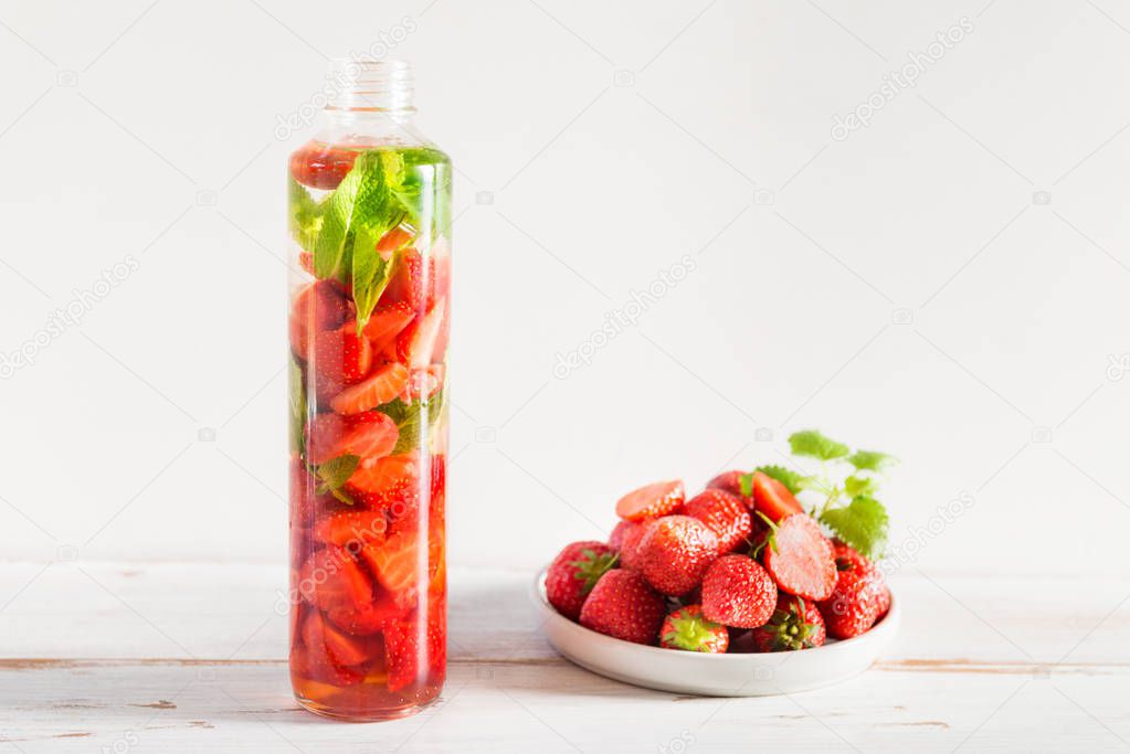 Detox Infused Water with Strawberries and Mint in Sports Bottle with Strawberries nearby on Light Background