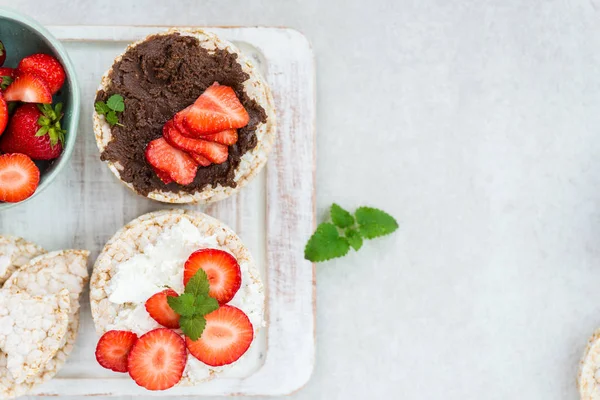 Pirinç kek Ricotta peynir, çikolata fındık yaymak ve ışık arka plan üzerinde çilek gibi malzemelerle gelen sağlıklı Snack