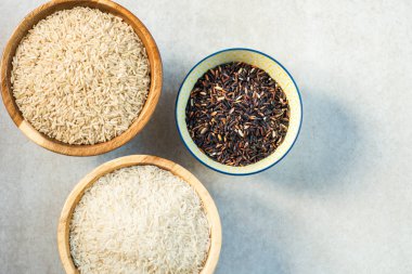 Pirinç ahşap kase basmati, kahverengi ve gri arka plan üzerinde siyah gibi farklı türleri