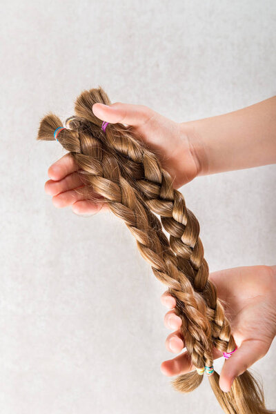 Hand is holding long hair as donation for kids charity, which makes wigs for cancer patients, light background