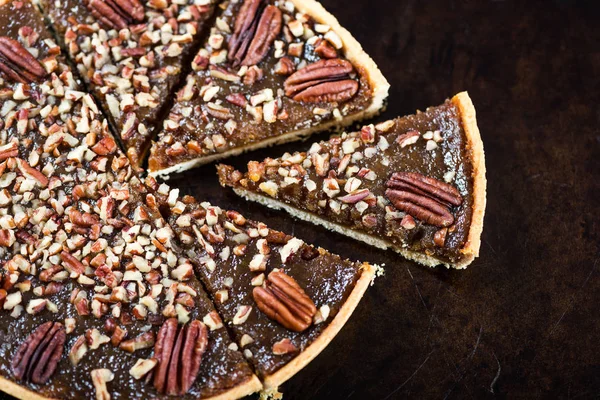 Pecan Pie, made from butter enriched pastry with golden syrup, maple sauce and breadcrumbs, topped with pecans, on dark background