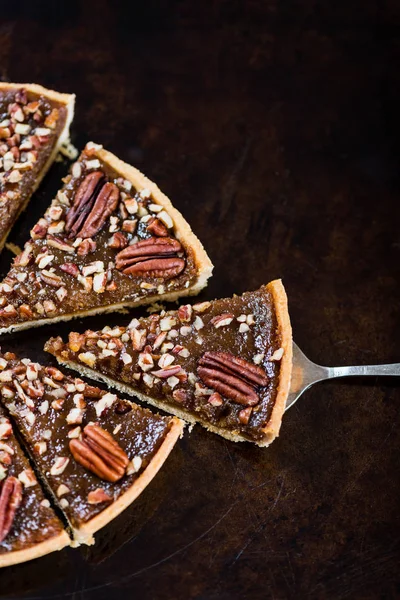 Pecan Pie, made from butter enriched pastry with golden syrup, maple sauce and breadcrumbs, topped with pecans, on dark background