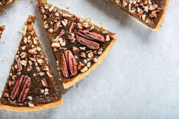 Pecan Pie, made from butter enriched pastry with golden syrup, maple sauce and breadcrumbs, topped with pecans on grey background