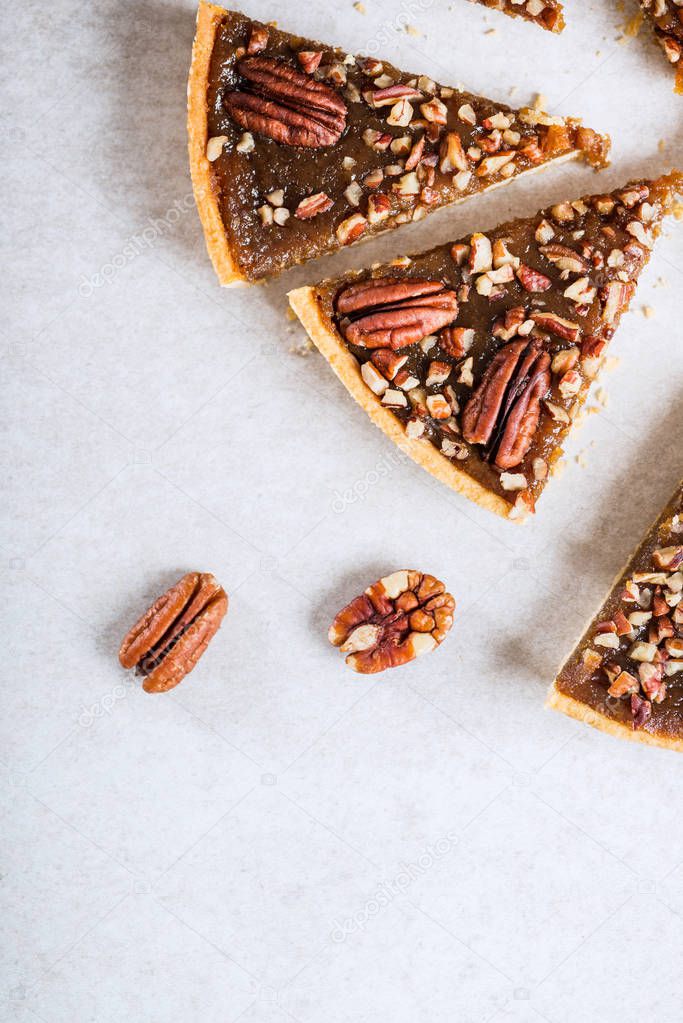 Pecan Pie, made from butter enriched pastry with golden syrup, maple sauce and breadcrumbs, topped with pecans on grey background
