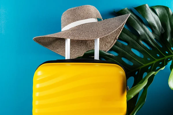 Bright and stylish cabin size suitcase with straw hat and monstera leaf