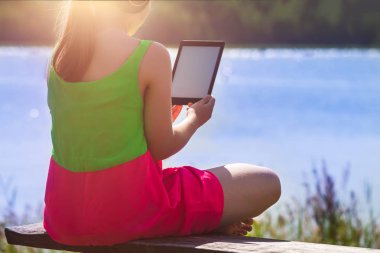 Genç kız deniz kenarında bankta ebook okuyor