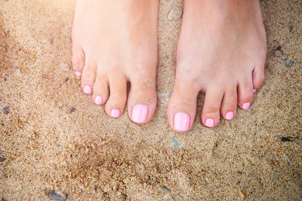 Fiatal hölgy megmutatja neki fény rózsaszín pedikűr körmök homokos strandon háttérben — Stock Fotó