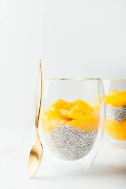 Ev yapımı 4 Mango Chia Pudingi. Beyaz arka planda çift cam bardakta badem ya da hindistan cevizi sütüyle yapılmış.