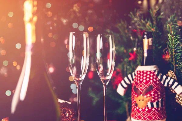 XmasやNew Year Partyに備えて 空のフルートグラスとシャンパンボトル2本を用意しました 背景にはクリスマスジャンパーとクリスマスツリーがあります — ストック写真