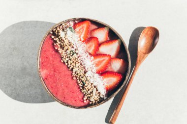 Muz ve çilekli Pembe Meyve Smoothie, üzerinde çilek parçaları, Granola ve Hindistan cevizi parçacıkları, üzerinde Hindistan cevizi kabuğu kabuğu kabuğu, güçlü gölgeler. Sağlıklı yaz kahvaltısı, manzaralı.