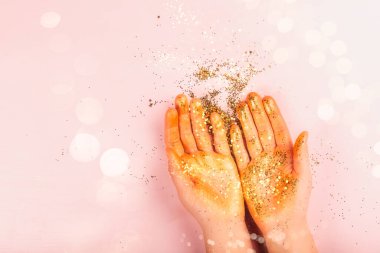 Güzel kadınların elleri pembe arka planda altın parıltıyla kaplıdır.