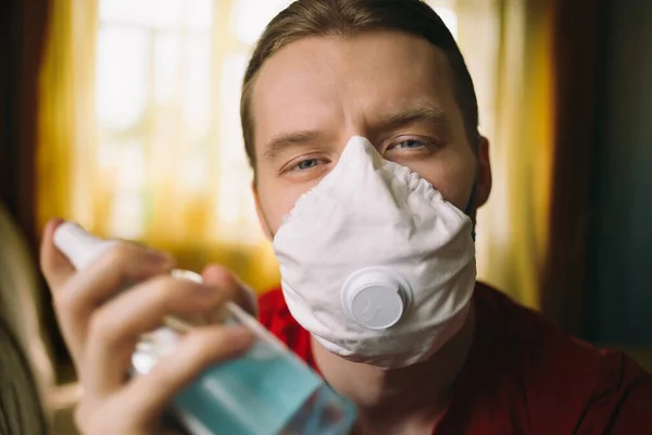 Koronavirüs maskeli ve elinde antiseptikle ciddi bir yüzü olan genç bir adamın portresi.