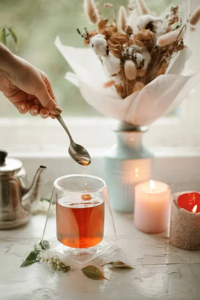 Çay demliyorum. Eski vitrinde siyah çay ve duble cam bardak. Elin kaşıkla çay damlatıyor. Vazodaki çiçekler ve arkadaki mumlar..