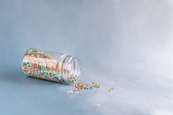 Cam kavanozdan dökülen renkli şekerleme, mavi arka planda pasta ve fırın süslemesi.