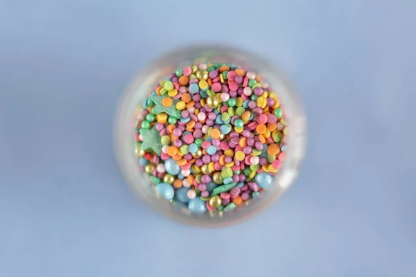 Cam kavanoza serpiştirilmiş renkli bir şekerleme, mavi arka planda pasta ve fırın dekorasyonu.