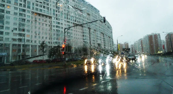 Şehir caddesinde, farları açık, yağmurda araba deresi.