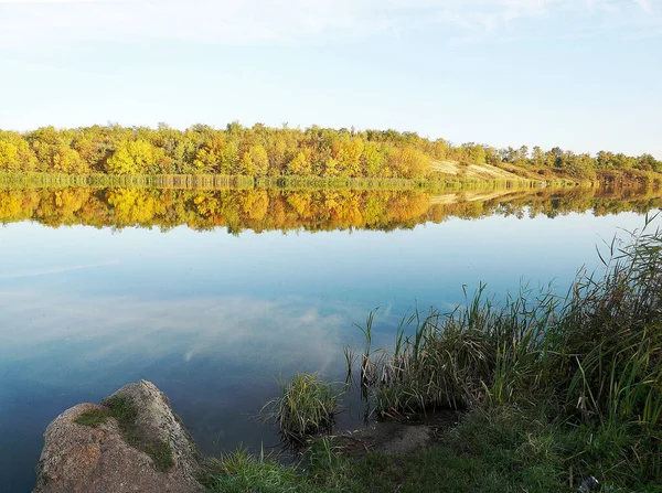  Nehrin iki yakası. Bir kıyıda taş ve sazlıklar, diğerinde sonbahar ormanı.