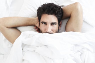 Adam beyaz çarşaf altında yatakta istirahat portre