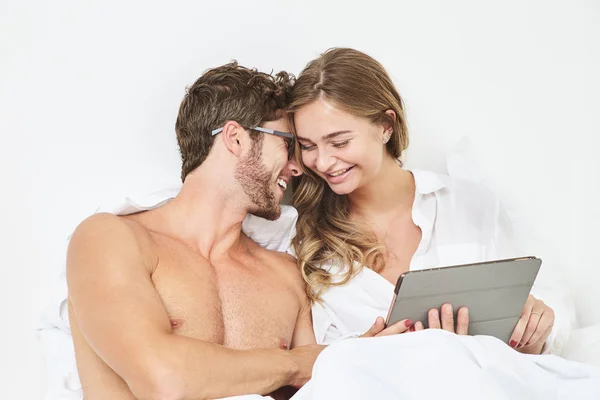 Smiling couple with tablet in bed