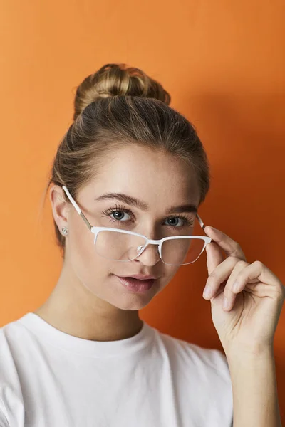 オレンジ色の背景にメガネを調整する女の子 — ストック写真