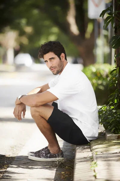 Thoughtful fellow sitting on curb, looking away