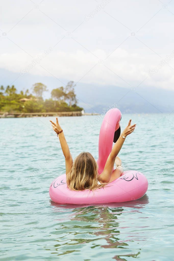 Girl in pink inflatable flamingo making peace signs at sea