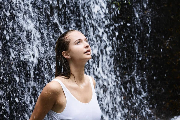 beautiful young woman under waterfalls, looking up
