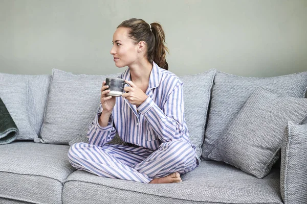 Pretty brunette in pj\'s on sofa with morning coffee