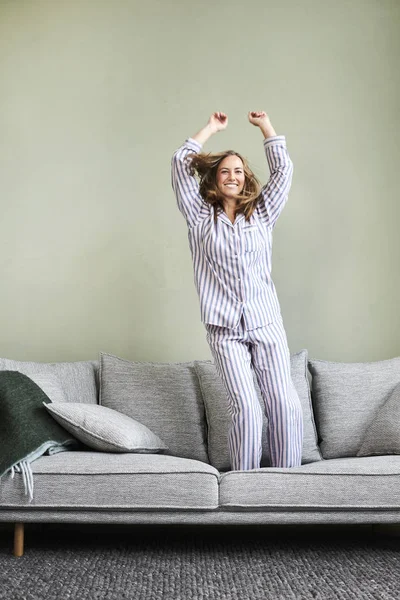 ソファに飛び乗るパジャマのかわいい女性 — ストック写真