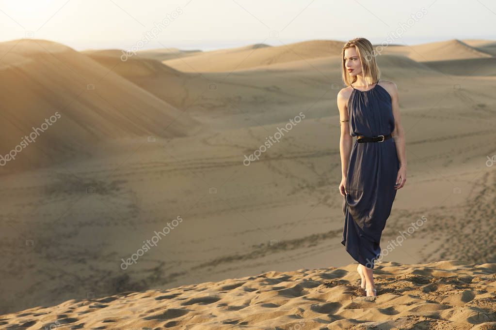 Glamorous woman in desert wearing blue dress, looking away