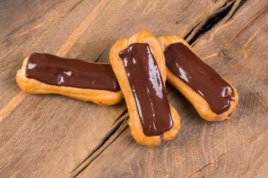 Eklerleri ahşap arka plan üzerinde çikolata tepesi ile.