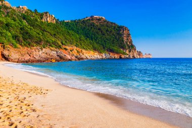 Kleopatra beach Alanya Yarımadası'nda, Antalya bölgesinde, Türkiye'nin yeşil taşlar ile deniz kıyısında. Güzel güneşli manzara ile turizm için temiz su ve kum. Uçurumdaki Alanya Kalesi